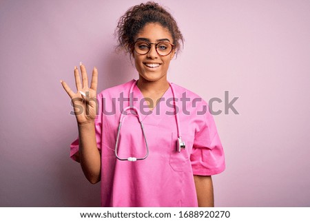 African american nurse girl wearing medical uniform and stethoscope over pink background showing and pointing up with fingers number four while smiling confident and happy.