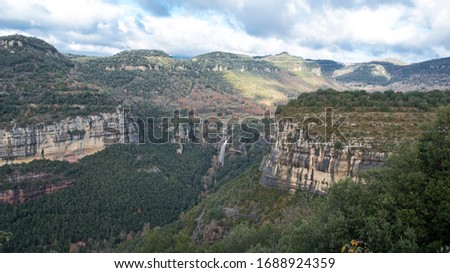Highlands with a natural waterfall and some cliffs. It is a partly cloudy autumn day in Rupit i Pruit, Catalunya, Spain, Europe. Royalty-Free Stock Photo #1688924359