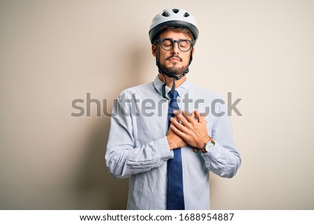 Young businessman wearing glasses and bike helmet standing over isolated white bakground smiling with hands on chest with closed eyes and grateful gesture on face. Health concept.