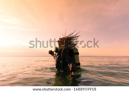 Female Scuba Dive Instructor Wearing a Dry Suit, a Twin Tank and Holding Fins Flipping Wet Hair in the Air Royalty-Free Stock Photo #1688959918