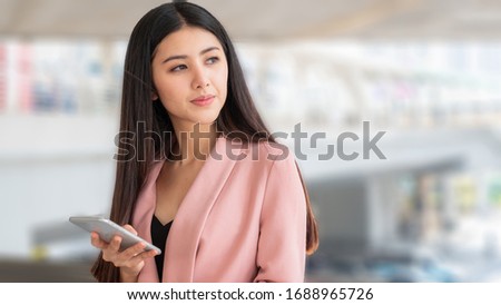 business asian woman hold smartphone and look on other side. with blurred outdoor background.