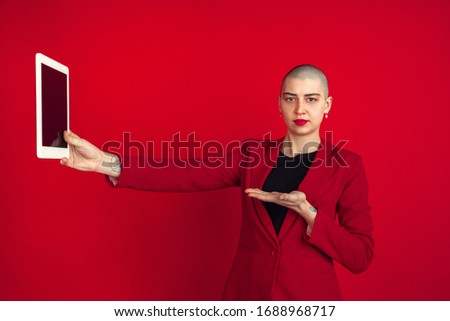 Taking selfie or vlog. Portrait of young caucasian bald woman isolated on red studio background. Beautiful female model in jacket. Human emotions, facial expression, sales, ad concept. Freaky culture.