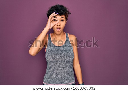 Young beautiful african american afro sportswoman doing exercise wearing sportswear doing ok gesture shocked with surprised face, eye looking through fingers. Unbelieving expression.