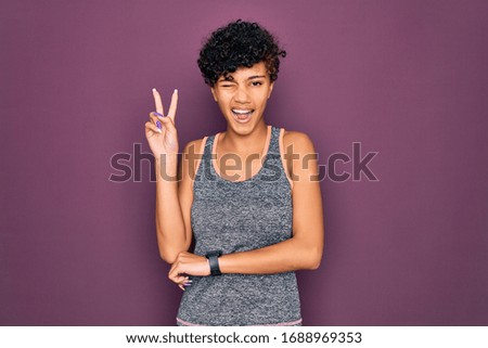 Young beautiful african american afro sportswoman doing exercise wearing sportswear smiling with happy face winking at the camera doing victory sign with fingers. Number two.