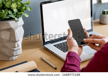 Close up of stylish composition with businessman, mock up laptop screen, cup of coffee, plants and office supplies in modern home office.