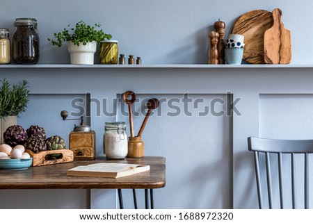 Stylish composition of kitchen interior with wooden family table, vegetables, herbs, plants, food supplies and kitchen accessories in gray concept of home decor. 