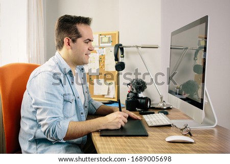 Boy photographer working from home on his computer. On the table are an electronic graphics tablet and a photo camera