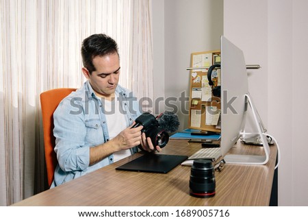 Boy photographer preparing his camera while working from home on his computer. On the table are an electronic graphics tablet and a photo camera