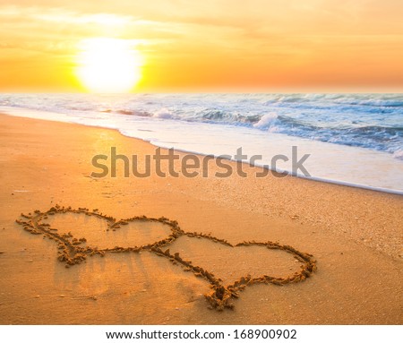 two hand drawn hearts on beach sand over sunset