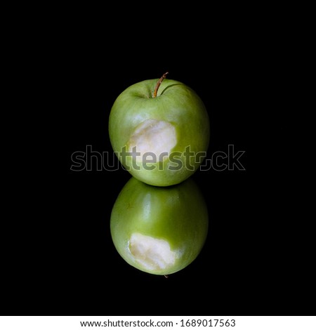 A still life of a green bitten apple on a mirror in  a flat black background