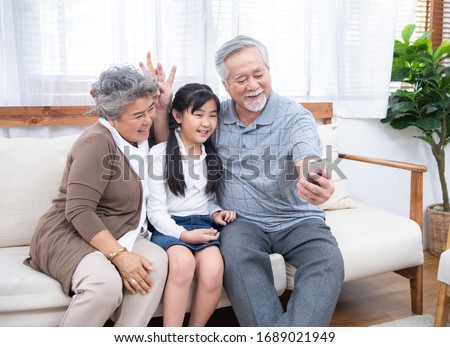 Asian Grandfather taking selfie with couple Grandparent and granddaughter with happy feeling by mobile phone in house, Long live and Elderly society, Warm family and stay at home,leisure life concept.