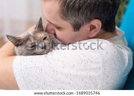 a man hugs a cat. hugs with a cat on the sofa in a room at home. home furnishings, mesosaline. stay at home with Pets. happy kitten in the hands of a man.