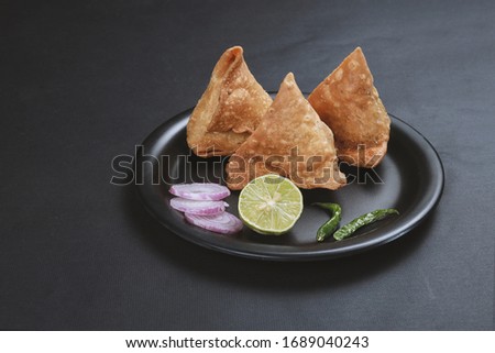 Indian samosas - fried/baked pastry with savoury filling, popular Indian snacks, served in black dish with sauce fresh onion and lemon cilantro on rustic background. Royalty-Free Stock Photo #1689040243