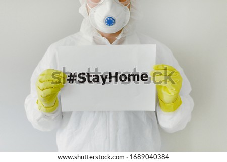 Doctor in protective clothes is holding an inscription stayhome and looking at the camera portrait closeup. Covid-19 protection. Pandemic, epidemic, vaccination concept. Working in laboratory. Royalty-Free Stock Photo #1689040384