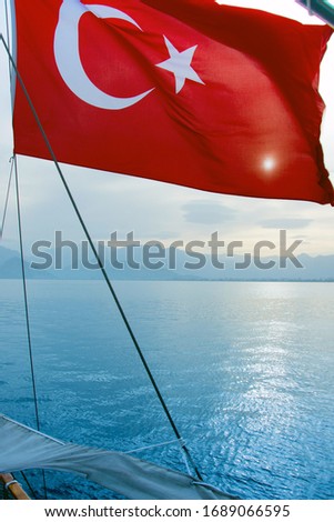 The Turkish flag unfolds in the wind above the water, Turkey, a red flag with a crescent moon and a star, the sun shines through the Turkish flag