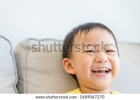 Happy toddler boy watching cartoon streaming and laughing at home.Self isolation stay at home from Covid-19 Coronavirus crisis.Kid boy showing front teeth with big smile and laughing.Pandemic covid19.