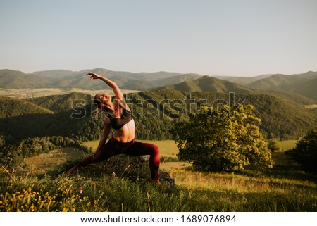 skinny young woman in leggings and sport bra is practicing yoga pose in beautiful landscape/nature by sunset