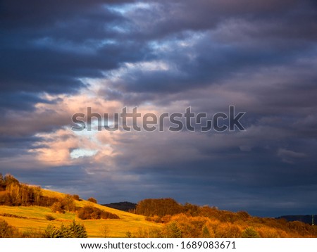 A rift in dense clouds in the sky above a hill in the evening lit by the sun