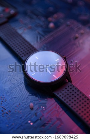 Smart watch with analog display and a black wrist strap on hitec hi tec computer motherboard background . With a 2 color lights red and blue.Close up