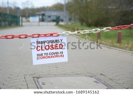 Red white chain barrier and sign with text Temporarily Closed due to Covid-19 Coronavirus, in front of a blurred company, countrywide pandemic lock down, copy space, selected focus Royalty-Free Stock Photo #1689145162