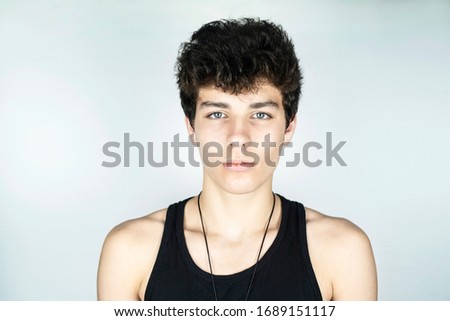 Handsome but sad teenage boy with dark hair on light background. The guy is ashamed to smile because he has braces on his teeth