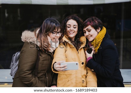 group of friends using mobile phone outdoors in the street. Happy women smiling. lifestyle and travel concept