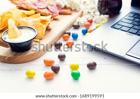 Working at home and snacks. Home office with unhealthy lifestyle. Leisure with laptop and fast food. Potato chips, pizza, candies and computer on the table.
