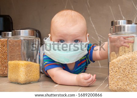 little boy in a protective mask on his face in the kitchen with a large supply of grain and flour for quarantine time