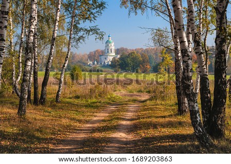 A country road, birch trees, a large field and a Church on a hill on a Sunny September day.