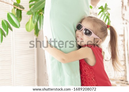 joyful three year old girl in a red dress and sunglasses hugs mom