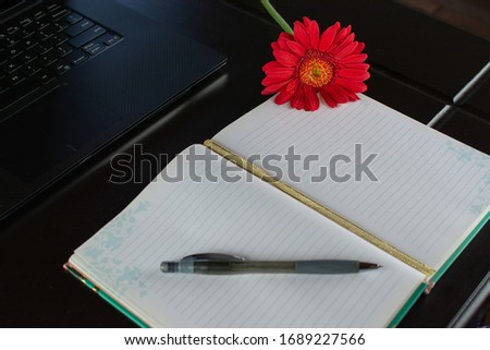 Notebook with a nice rose and laptop on wooden table