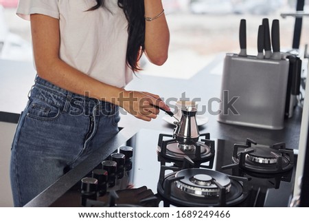 Close up view pf young beautiful brunette in casual clothes that preparing coffee in kitchen at daytime.