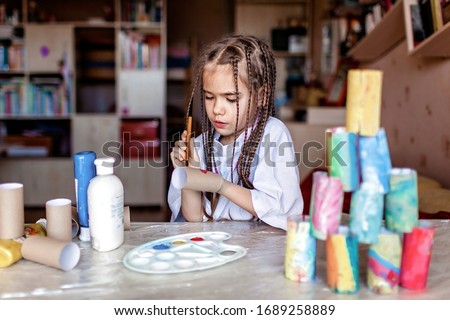 Cute girl coloring toilet paper rolls to use them as if paper blocks to build a tower, home activity during lockdown, do it yourself and zero waste concept Royalty-Free Stock Photo #1689258889