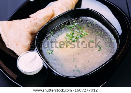 Fresh fish soup with egg in a black deep dish with pancakes and sour cream on a black background, front view. Blue wooden background
