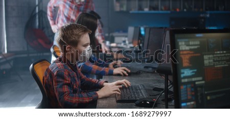 Medium shot of a male student and a teacher in face masks discussing programming in school