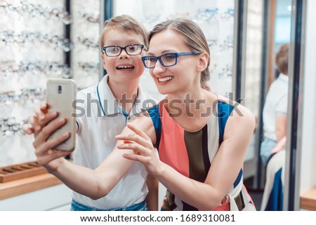 Mother and son taking selfie with new glasses at optometrist shop being happy