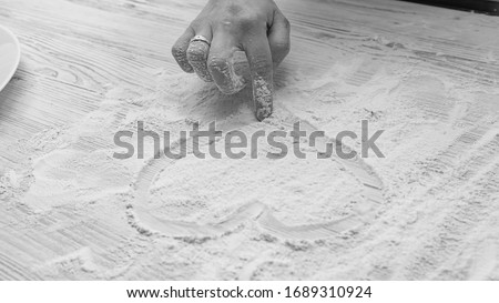 female hand draws heart on flour