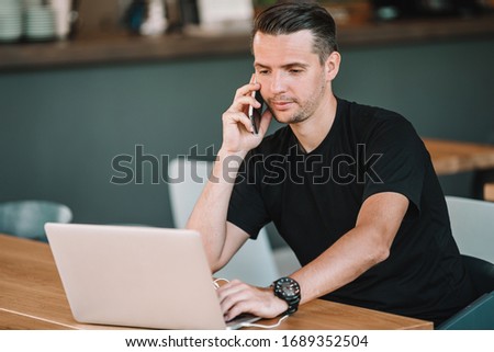 Young man working at laptop in outdoor cafe drinking coffee. Man using the smartphone