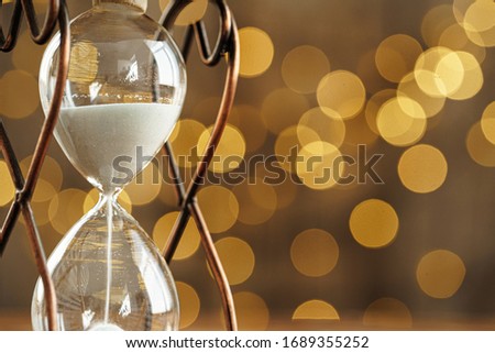 Hourglass on wooden desk against  blurred lights background