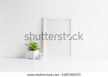 Plant in marble pot with photo frame near white wall.