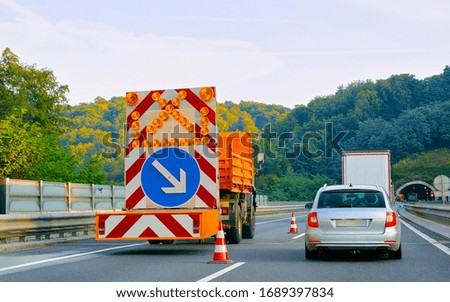 Truck carrying arrow down left reflective direction road sign in highway in Poland.