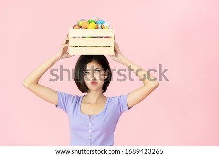 Cheerful Asian pretty girl holding up a wooden basket with colorful Easter eggs inside. Colourful Easter eggs in the festival celebrating. Cute girl's portrait in Easter egg festival concept.