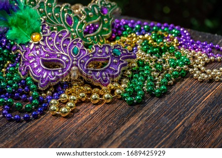 Mardi Gras color beads with masks on wooden table in sunlight Royalty-Free Stock Photo #1689425929