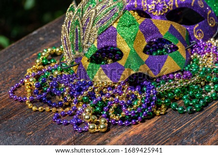 Mardi Gras color beads with masks on wooden table in sunlight