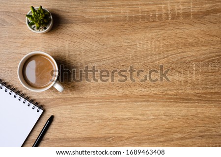 desk office with blank notepad, coffee cup and pen on wood table. Flat lay top view copy spce.