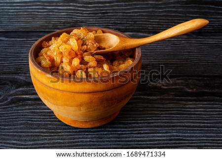Golden raisins in wooden bowl on dark background, rustic