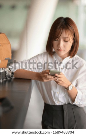 Cropped shot of young female photographer using smartphone to contact her customer 
