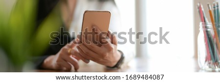 Cropped shot of female freelancer using smartphone to relax form her work while sitting in workspace