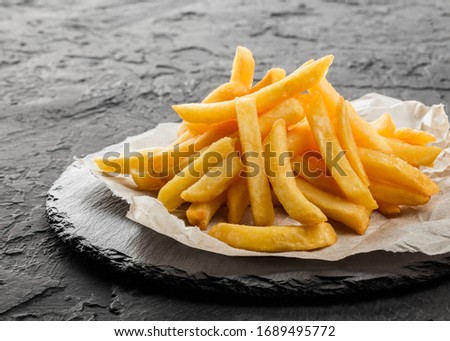 Tasty french fries potatoes on paper over black stone background. Hot fast food, close up Royalty-Free Stock Photo #1689495772