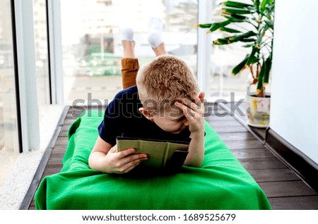 Child boy reads an e-book on a tablet and watches cartoons. Isolation from the outside world. World Quarantine, Coronovirus Pantemia, COVID-19. Close-up. The child is sitting on the balcony. To stay
